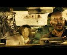 Screen shot from Witching and Bitching with two men in the front of a car, one painted silver.