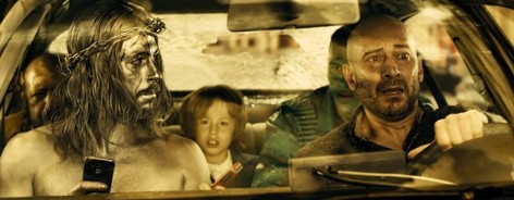 Screen shot from Witching and Bitching with two men in the front of a car, one painted silver.