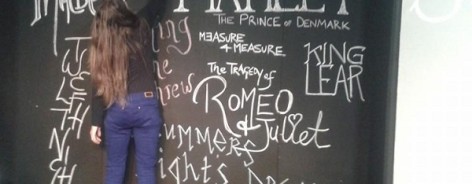 Photograph of a woman in blue trousers writing up productions on a blackboard