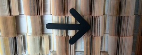 Photo of a wall of books with their pages played and a black arrow pointing to the right