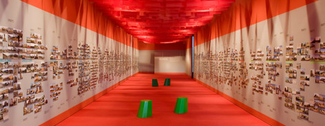 Photo of a long corridor with white walls, plastered with photos, and an orange ceiling and floor.