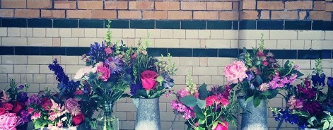 Photo of bouquets in jugs against a painted brick wall.