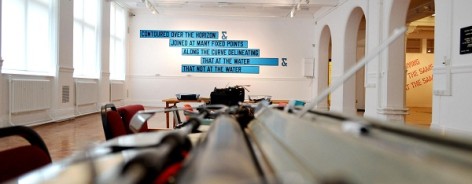 Photo along a row of typewriters, with a text art work on the back wall