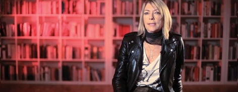 Photo of Kim Gordon with red bookshelves behind her