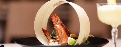 Photo of a prawn on a black plate next to a cocktail