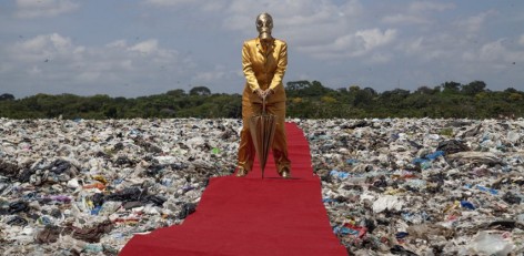Man in gold with gask mask stands on red carpet over trash