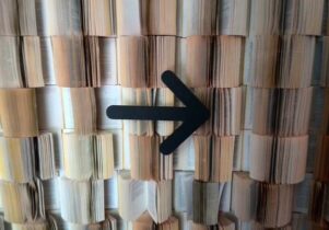 Photo of a wall of books with their pages played and a black arrow pointing to the right