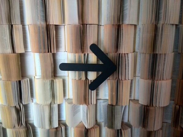 Photo of a wall of books with their pages played and a black arrow pointing to the right
