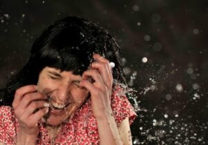 Photo of a girl in a pink top having water splashed in her face.