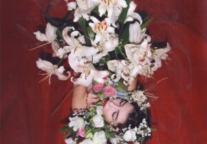 Photo of Edith holding a huge bunch of lillies, with a red back drop