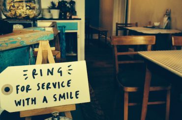 Photo of a handwritten label in a cafe that says "Ring for service with a smile"