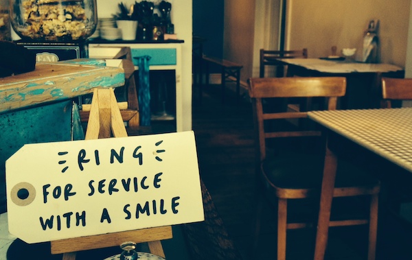 Photo of a handwritten label in a cafe that says "Ring for service with a smile"