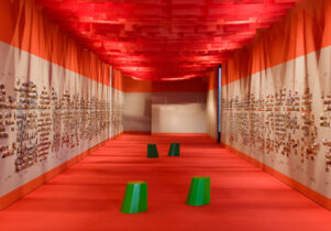 Photo of a long corridor with white walls, plastered with photos, and an orange ceiling and floor.