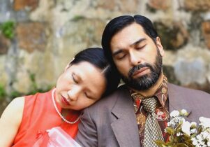 Photo of the artist next to a woman in red, who leans her head on his shoulder