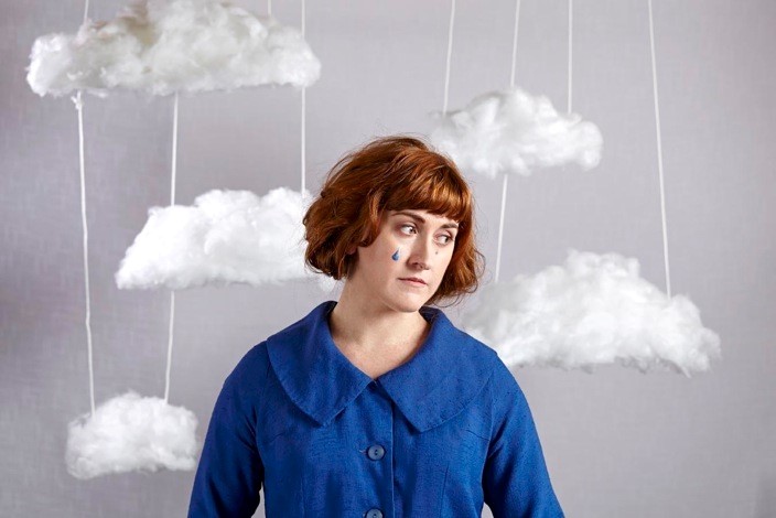Photo of musician Liz Green in a blue jacket with handmade clouds hung around her
