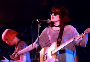 Photo of the lead singer of PINS with her guitar, wearing sunglasses