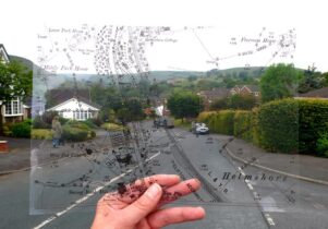 A hand holds a transparent map up to a countryside road