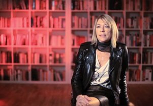 Photo of Kim Gordon with red bookshelves behind her