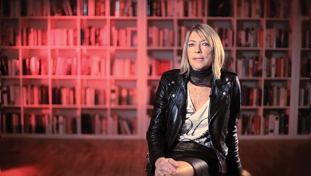 Photo of Kim Gordon with red bookshelves behind her