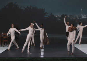 People in white body suits pose on a theatre set
