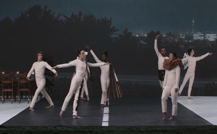People in white body suits pose on a theatre set