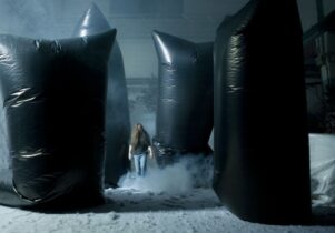 Long haired man amongs snow and black plastic sculptures