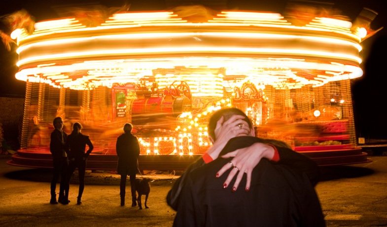 Photo of a couple kissing in front of a carousel