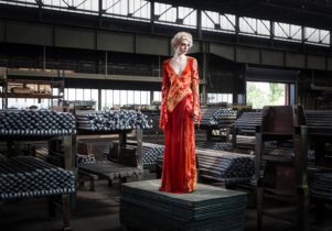A woman in a red dress stands in a warehouse