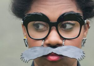 Woman wears glasses and a fake moustache