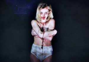 A girl stands in pants with blood on her face