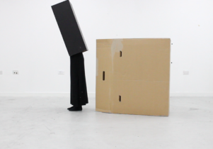 Image of person in a black box, with a cardboard box beside