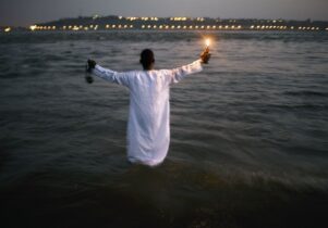 Man in white smock holds up a candle outside