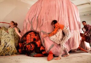 Photo of performers moving a large pink sculpture