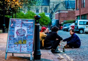 A billboard and people sitting on the pavement