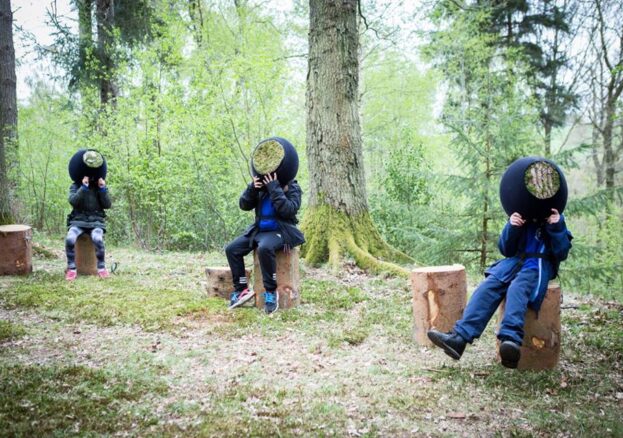 Photo of children sitting on tree stumps wearing headgear