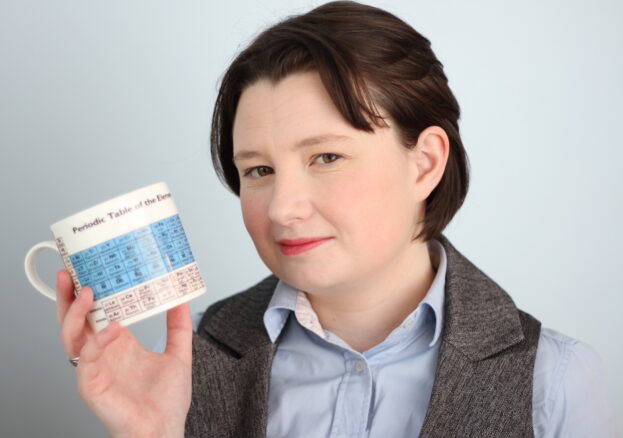 Photograph of poet and scientist Rachel McCarthy holding a mug showing the periodic table of elements.