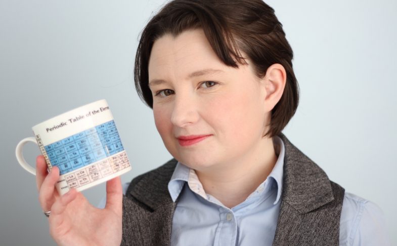 Photograph of poet and scientist Rachel McCarthy holding a mug showing the periodic table of elements.