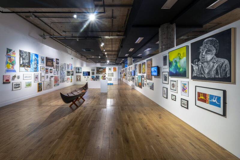 View of the Manchester Open 2022 exhibition, with wooden floor and paintings covering walls from floor to ceiling.