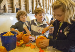 Three children pumpkin carving at a table