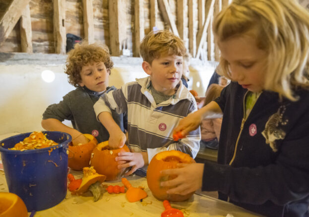 Three children pumpkin carving at a table