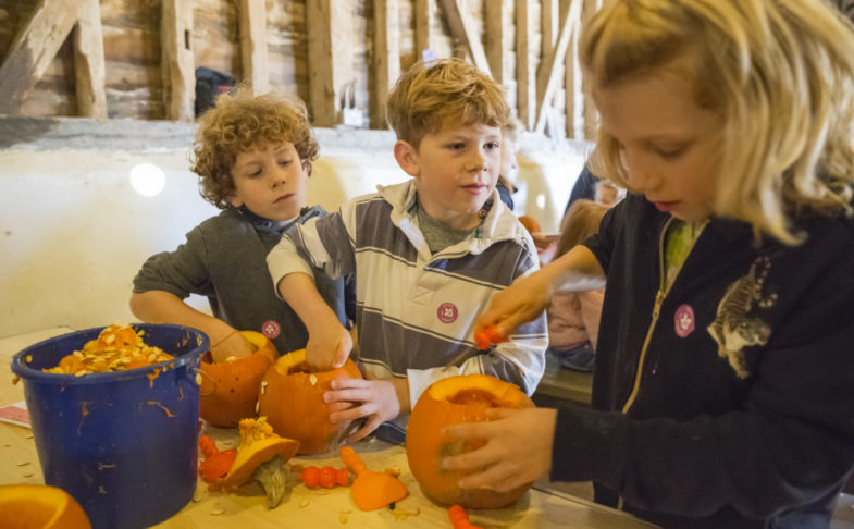 Three children pumpkin carving at a table