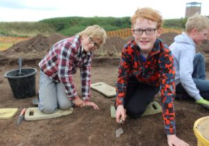 Children getting involved in the Junior Archaeology Finds event. They're using trowels to scrape layers of soil away.