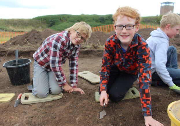 Children getting involved in the Junior Archaeology Finds event. They're using trowels to scrape layers of soil away.