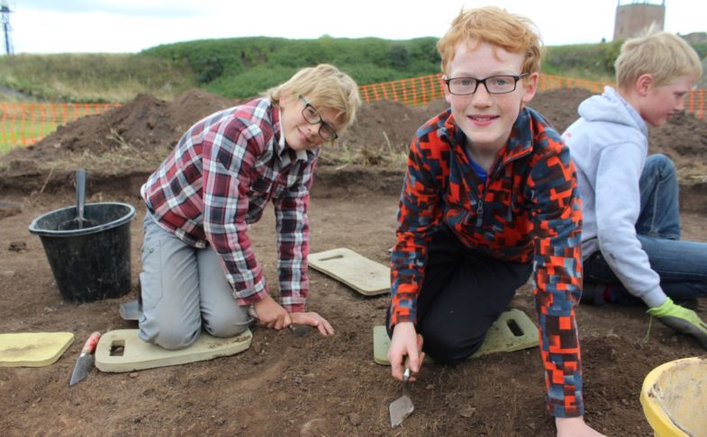 Children getting involved in the Junior Archaeology Finds event. They're using trowels to scrape layers of soil away.