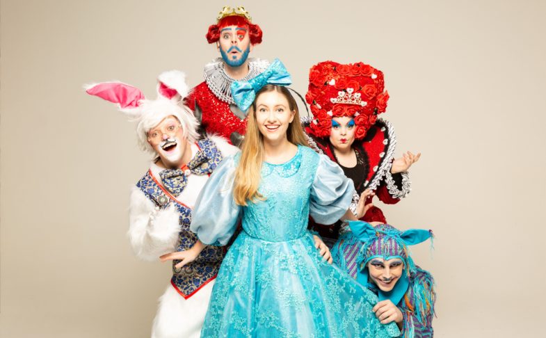 Alice in Wonderland at Waterside Arts. Alice is shown in a blue dress characters from the story behind her including the white rabbit and the Queen of Hearts. Part of our half term in Manchester activities