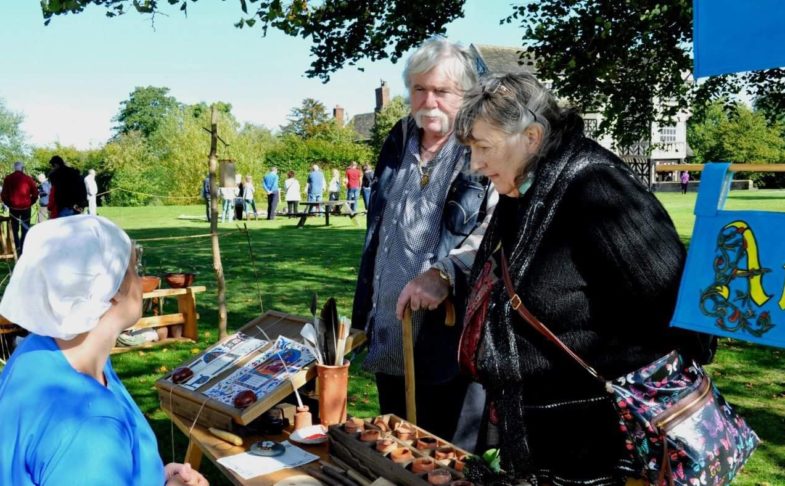 Living history event at Little Moreton Hall. A lady in period dress sits at a desk talking to visitors in the outdoors.