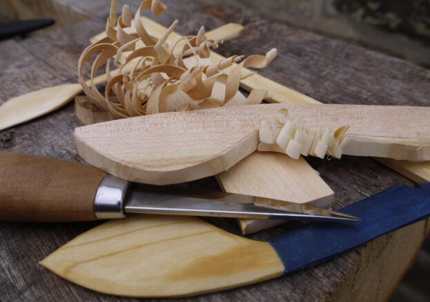 Items carved in the Carving and Campfires events shown on a wooden table along with wooden shavings