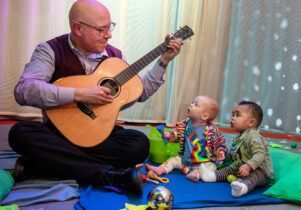 Babies listening to a man play the guitar as part of My First Protest Song