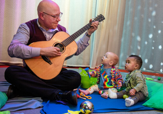 Babies listening to a man play the guitar as part of My First Protest Song