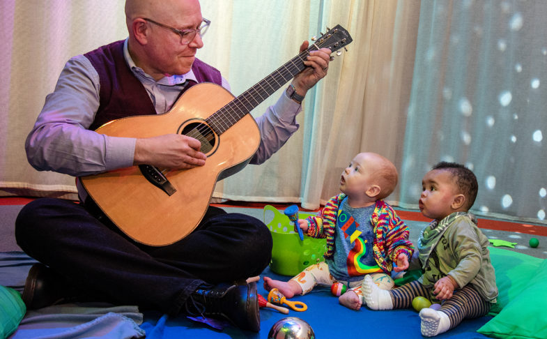 Babies listening to a man play the guitar as part of My First Protest Song
